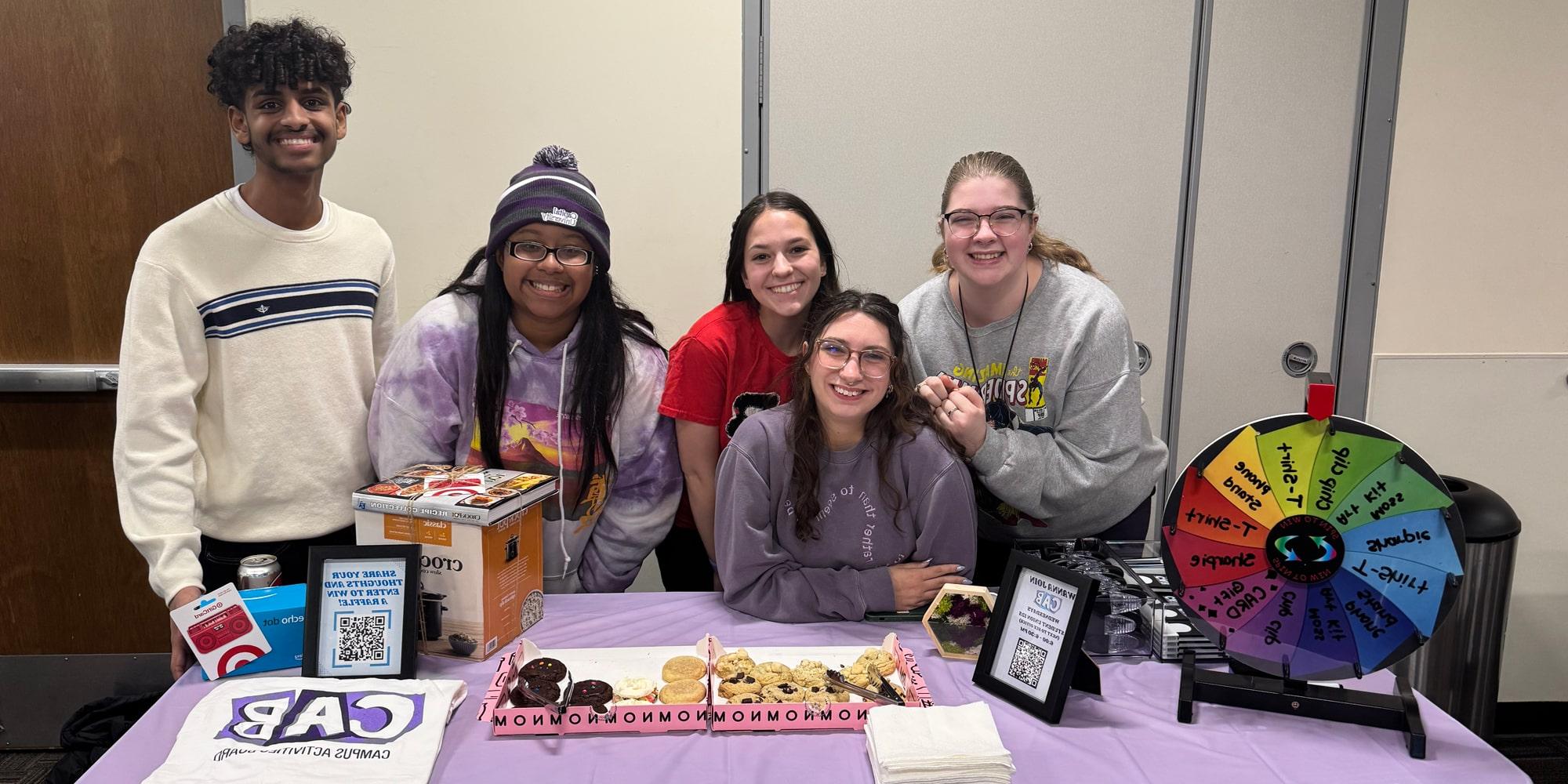 A group of students in CAB sit behind a welcome table smiling